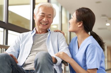 young friendly asian female caregiver talking to elderly man in 