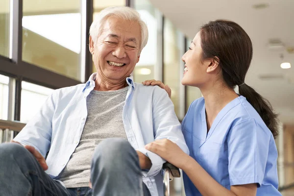 Young friendly asian female caregiver talking to elderly man in — Stock Photo, Image