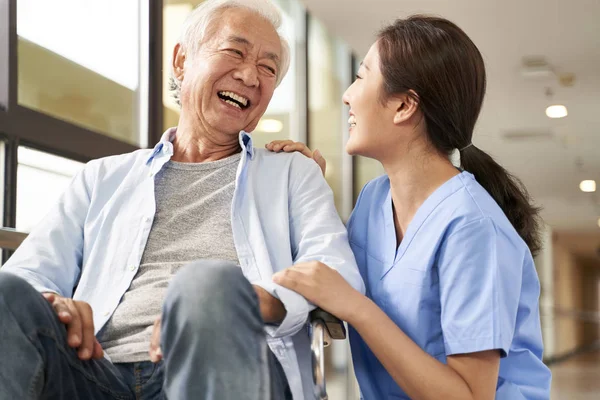 Young friendly asian female caregiver talking to elderly man in — Stock Photo, Image