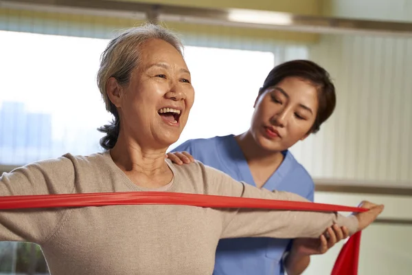 Asiático velha mulher exercitando usando resistência banda no centro de reabilitação — Fotografia de Stock