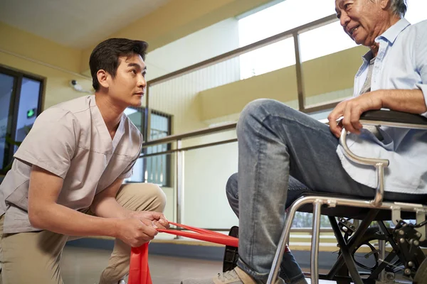 Jonge aziatische fysiotherapeut werken met senior patiënt met behulp van — Stockfoto