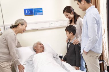 Çocuklu Asyalı bir aile dedelerini hastanede ziyaret ediyor.