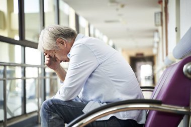 asian old man sitting in hospital hallway looking sad and depressed