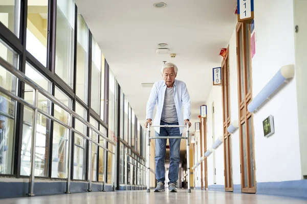 senior asian man walking using a walker in hallway of nursing home