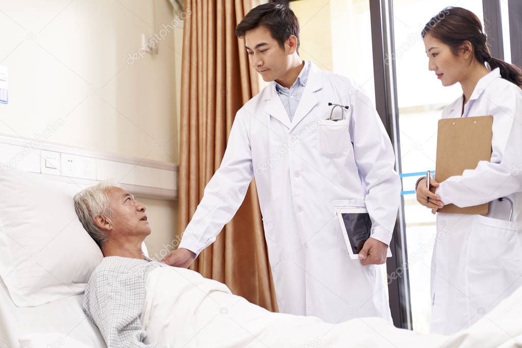 senior asian man male patient lying on bed talking to doctors in hospital ward