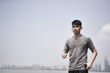 Genç Asyalı yetişkin adam deniz kenarında koşmaya hazır.