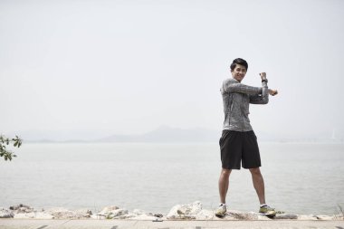 Genç Asyalı yetişkin adam deniz kenarında kollarını açıyor.