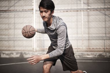 Genç Asyalı erkek basketbolcu dışarıda top tutmada pratik yapıyor.