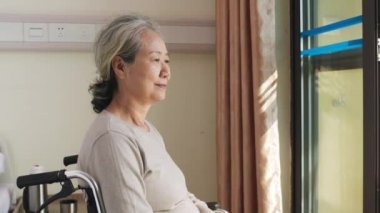 Huzurevindeki odasında tekerlekli sandalyede oturan Asyalı yaşlı kadın mutlu ve mutlu görünüyor.