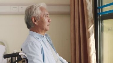 Asyalı yaşlı adam huzurevindeki odasında tekerlekli sandalyede oturuyor. Mutlu ve mutlu görünüyor.