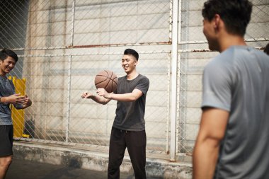Genç Asyalı yetişkin erkekler dışarıda basketbol oynarken eğleniyorlar.