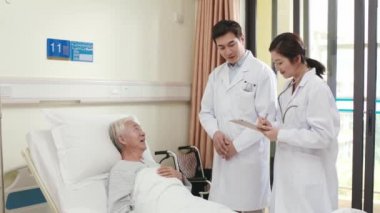 İki genç Asyalı doktor hastane koğuşunda kıdemli hastalarla konuşuyorlar.