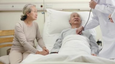 İki genç Asyalı doktor kıdemli hastayı muayene ediyor ve sağlık durumunu bildiriyor.