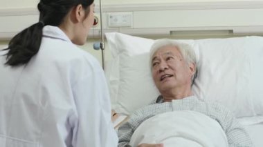 Dost canlısı genç Asyalı kadın doktor hastane koğuşunda erkek kıdemli hastayla konuşuyor.