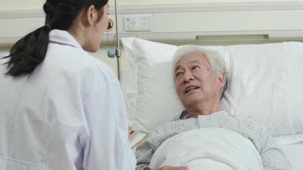 友好的亚洲年轻女医生在医院病房的床边与老年男性病人交谈 — 图库视频影像