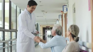 Genç Asyalı doktor yaşlı çifte hastane koridorlarında test sonuçlarını söylüyor.