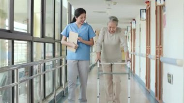 Genç Asyalı fizyoterapist son sınıf öğrencisiyle rehabilitasyon merkezinde ya da huzurevinde yürüyen birini kullanarak yürüyor.