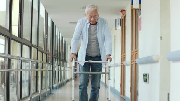 老人ホームの廊下で歩行者の助けを借りてゆっくり歩くアジア系男性 — ストック動画