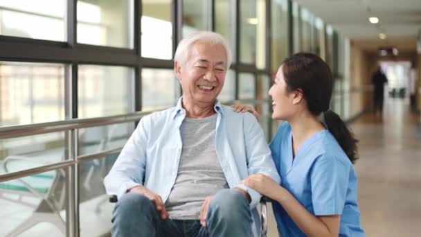友好的亚裔工人与住在辅助生活设施走廊的坐轮椅的老人交谈 — 图库视频影像