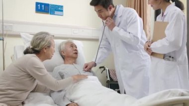 Genç Asyalı doktor hastane koğuşunda steteskop kullanarak kıdemli hastaları muayene ediyor.