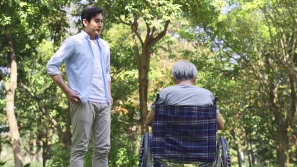 若いアジア系の大人の息子が車椅子で話してる屋外の公園で父親が死亡 — ストック動画
