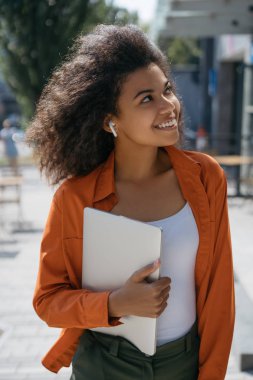 Mutlu başarılı serbest çalışan sokaklarda yürüyor, müzik dinliyor, modern kablosuz kulaklıklar kullanıyor, gülüyor. Genç duygusal iş kadını portresi dizüstü bilgisayarı tutuyor, dışarıda duruyor. 