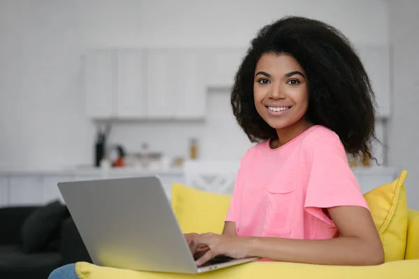 African American woman using laptop computer and internet, shopping online, ordering food, booking tickets,  sitting at home. Happy student studying, learning language, online education concept