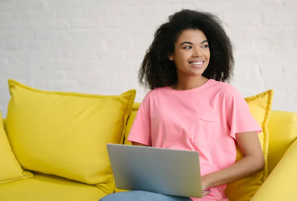 Happy emotional student studying, learning language, exam preparation sitting on yellow sofa. Successful woman copywriter working freelance project, using laptop and internet . Successful business and career