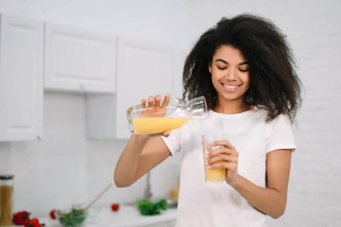 Genç ve güzel bir Afro-Amerikan kadın elinde portakal suyuyla bardak tutuyor. Sağlıklı yaşam tarzı konsepti, mutfakta doğal organik kahvaltı.
