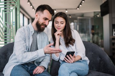 Kanepede otururken akıllı telefon ve mobil uygulama kullanan yakışıklı bir adam ve güzel bir kadın. İnternetten yemek sipariş eden, bilet ayırtan, seyahat planlayan, evde iletişim kuran çiftler.