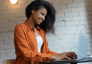 Serbest çalışma projesinde çalışan başarılı genç metin yazarının portresi. Neşeli Afrikalı Amerikalı kadın dizüstü bilgisayar kullanıyor, bilgi arıyor, klavyede daktilo kullanıyor, modern ofiste oturuyor.