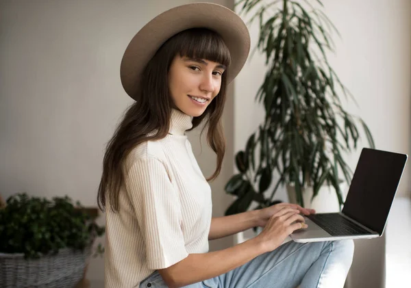 ラップトップコンピュータを使用して キーボードを入力して リモートでフリーランスのプロジェクトを作業美しい女性のコピーライター ヒップスターの帽子をかぶって創造的なデザイナーの肖像画は 計画を開始し 職場に座って笑っています 成功したビジネスとキャリアの概念 — ストック写真