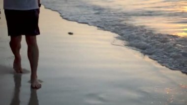 Portre, genç mutlu adamın canlı günbatımı sırasında tenha tropikal plaj tatil cenneti üzerinde yürüyüşünü takip ediyor.