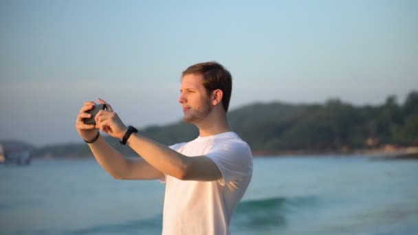 観光客スマートフォンでカラフルな夕日の間に熱帯島のビーチや海の休日の写真を撮る — ストック動画