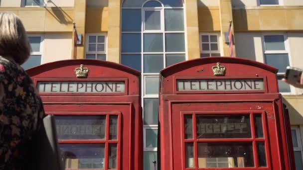 Nahaufnahme Zweier Roter Telefonzellen Während Die Menschen Vor Ihnen Gehen — Stockvideo