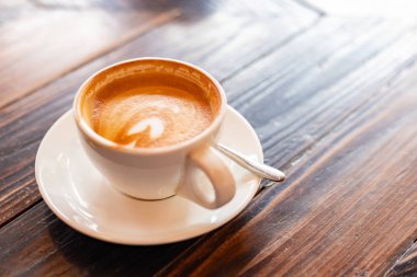 Sabahları tahta bir yüzeyde sunulan kalp şeklinde latte desenli bir fincan kahve..