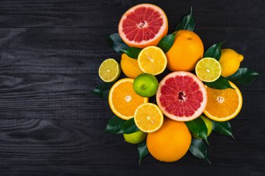 Turunçgiller, greyfurtlar, limonlar, portakallar, yeşil yapraklı limonlar kahverengi bir ahşap masada yatar. Yukarıdan görünüm