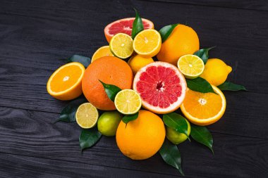Turunçgiller, yarım greyfurtlar, limonlar, portakallar yeşil yapraklı limonlar kahverengi ahşap bir masada yatıyor.