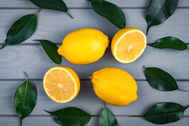 Bütün ve dilimlenmiş sulu limonlar gri bir masada yeşil yapraklarla kaotik bir şekilde uzanır..