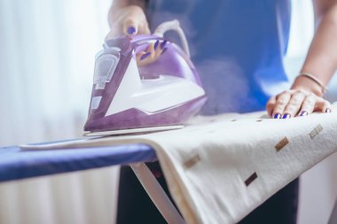 Kız feribotla ütü masasında ütü yapıyor. Apartman temizliği. Başarının saflık anahtarı. Mavi tişört ve beyaz ütü.