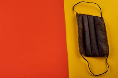 Çok renkli kağıt arka planda tıbbi siyah maske. Pastel turuncu ve sarı arka plan. Renkli. en üstteki görünüm