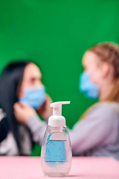 disinfectant fights bacteria. a daughter wearing a blue medical mask dresses her mom \'s mask. green background pink table. covid-19. protect the health. hygiene and quarantine