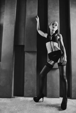Duvarın arkasında duran seksi bir mankenin portresi. Güneş ışığı. Siyah moda keten giymiş ince bir kız. BW. Tam yükseklikte güzel bir portre. Elini yukarı kaldırdı..
