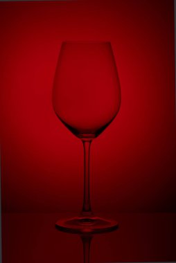 Kristal cam, yansıtıcı yüzeyde kırmızı bir zemin üzerinde duruyor. Stüdyo fotoğrafı Ürün. Şarap kadehinden güzel bir gölge. makro fotoğraf.