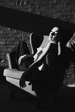 Güzel bir esmer kız, stüdyoda bir model. Güneş ve gölge. Sandalyeye oturur. Siyah, beyaz fotoğraf. Gözler kapalı..