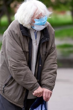 İki tıbbi maske takmış yaşlı bir dede ellerinde bir sopayla, aşırı büyümüş saçlarıyla ve kaşlarıyla para istiyor. Mağaza girişinin dışında bir dilenci. Zavallı adam. Karantinaya alındı. covid-19.