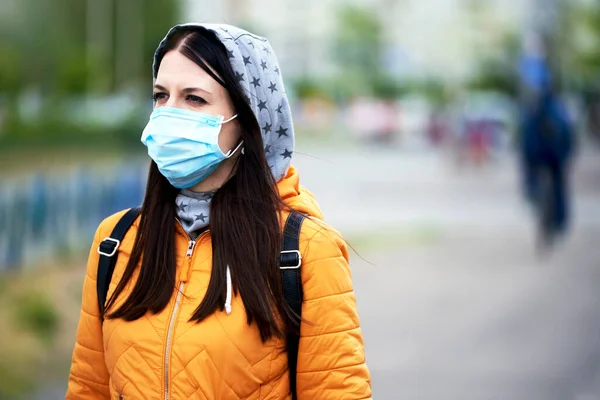 Tıbbi maskeli, kapüşonlu ve çantalı bir kız, geleceğe bakıyor. Hey turuncu ceketli. Karantinanın bitmesini bekliyor. Covid-19 'dan bıkmıştı. güzel ışık.