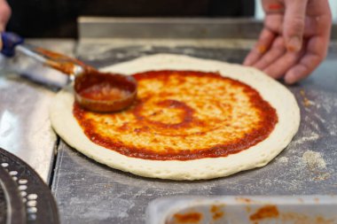 Şefin eli pizzaya pastörize domates ezmesi sürüyor.