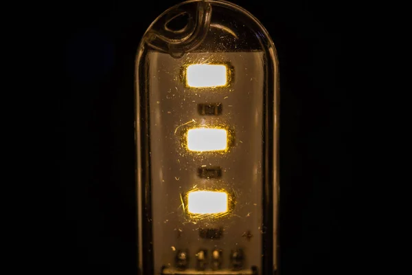 A lâmpada LED queima no escuro com uma luz amarela quente — Fotografia de Stock
