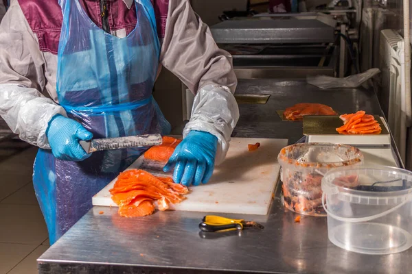 Fish production. Worker cuts fish with a knife into pieces for packaging — Stock Photo, Image